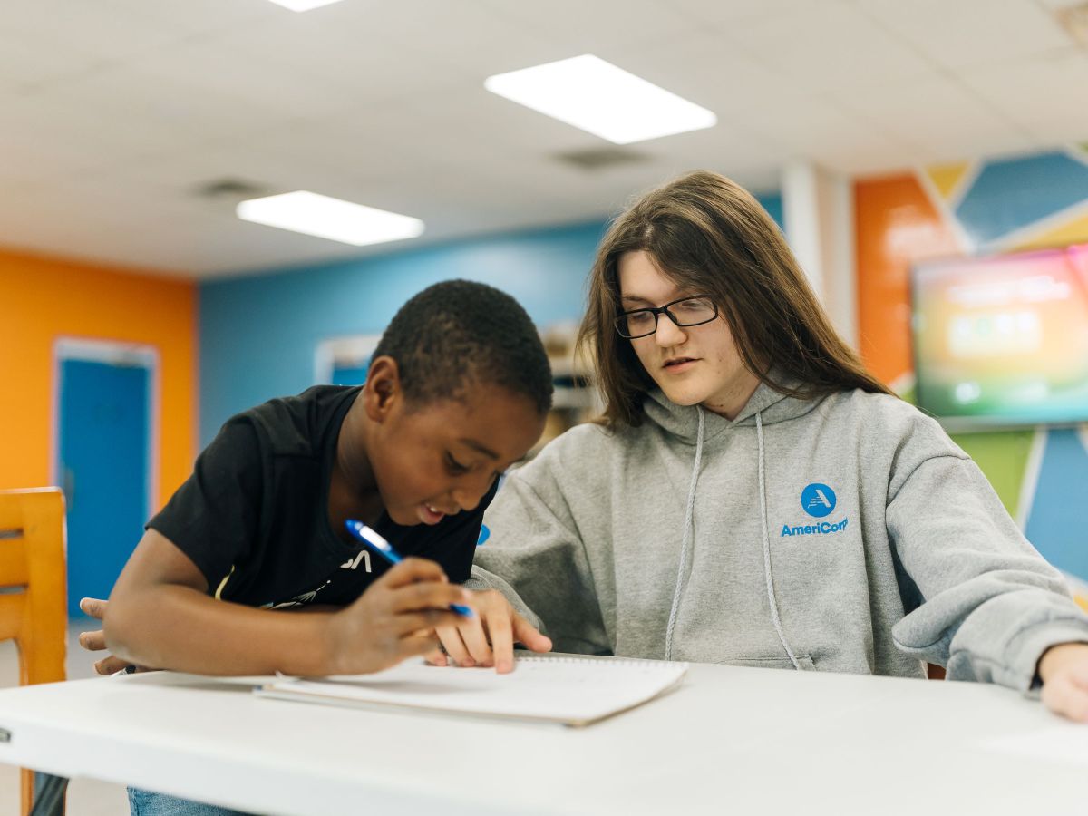 A volunteer helps a young student with homework in a classroom