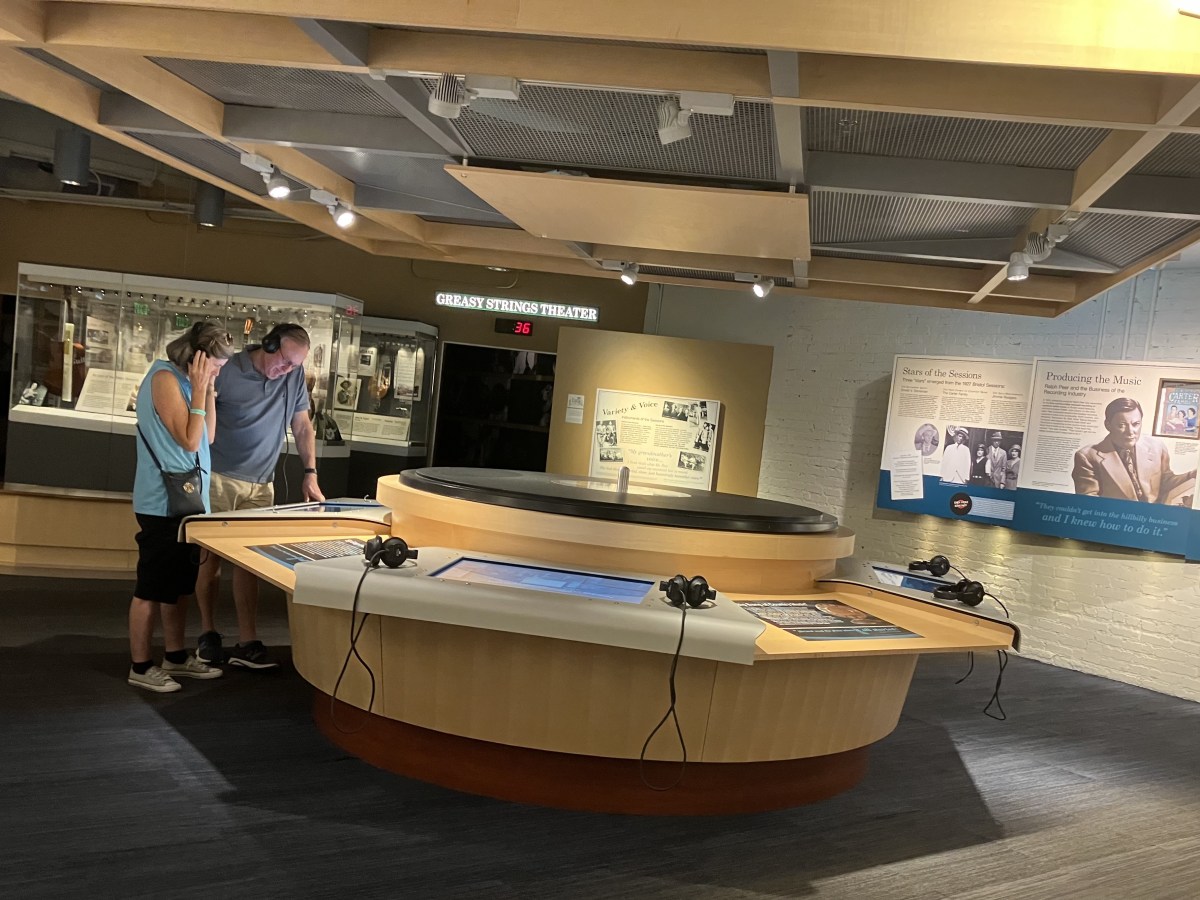 Two people stand in the middle of the Birthplace of Country Music Museum wearing headphones.