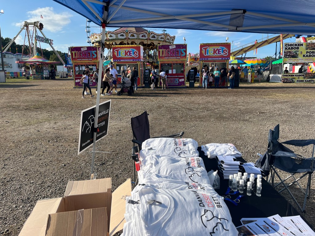 A Danville Deserves Better tent with t-shirts, signage, flyers and other items at the Danville-Pittsylvania County Fair.