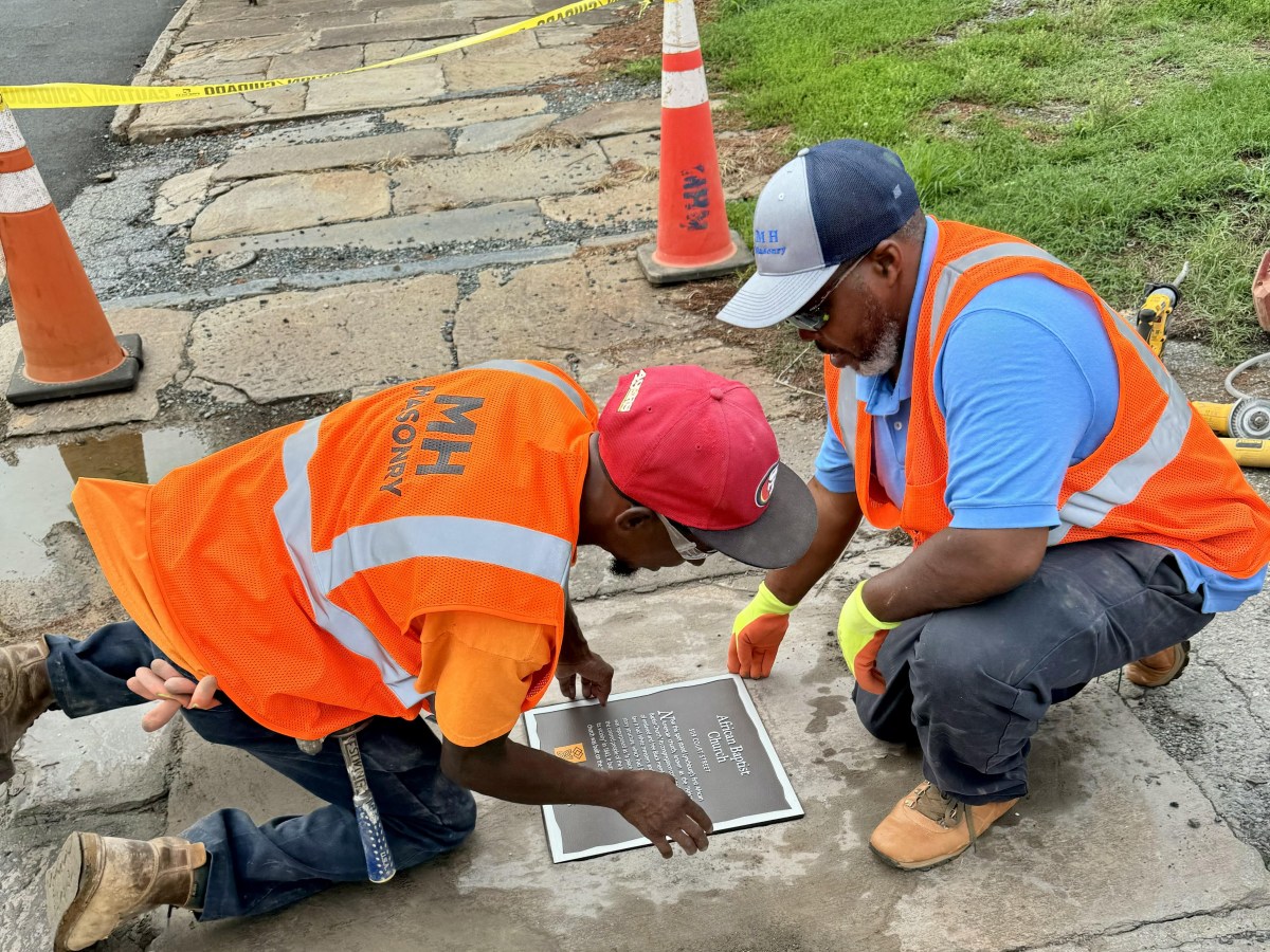 Adam Anderson (left, in red hat) and Damon Sims install one of the Silent Witnesses plaque. They both work for MH Masonry, which donated the labor for installation. Photo by David Neumeyer.